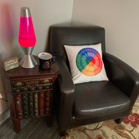 Gallery Photo of My spot, replete with Feelings Wheel back support pillow, a rather queer mug, and my lava lamp (purchased circa 1993 and still flowing!).