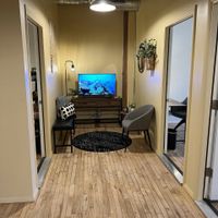 Gallery Photo of Waiting area between offices 2 and 3 - centered dark carpet, puffed bench and chair, wood furniture with tv screen showing ocean/corals.