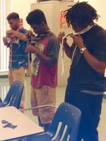 Gallery Photo of Three young men from our vilMENay Mentoring way learning how to correctly tie a necktie.