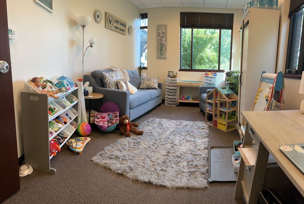 The playroom is a welcoming space with views of a pond and trees. It is filled with toys, games, fidgets, sand tr, a doll house and art space!