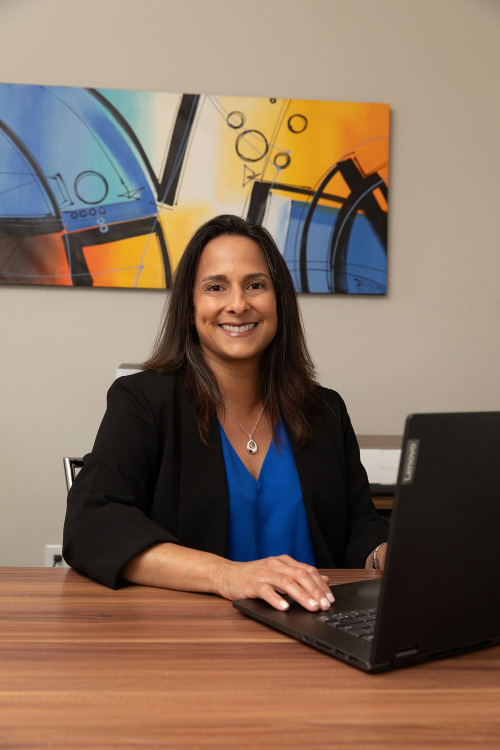 Latina smiling while sitting at a desk with a laptop open.