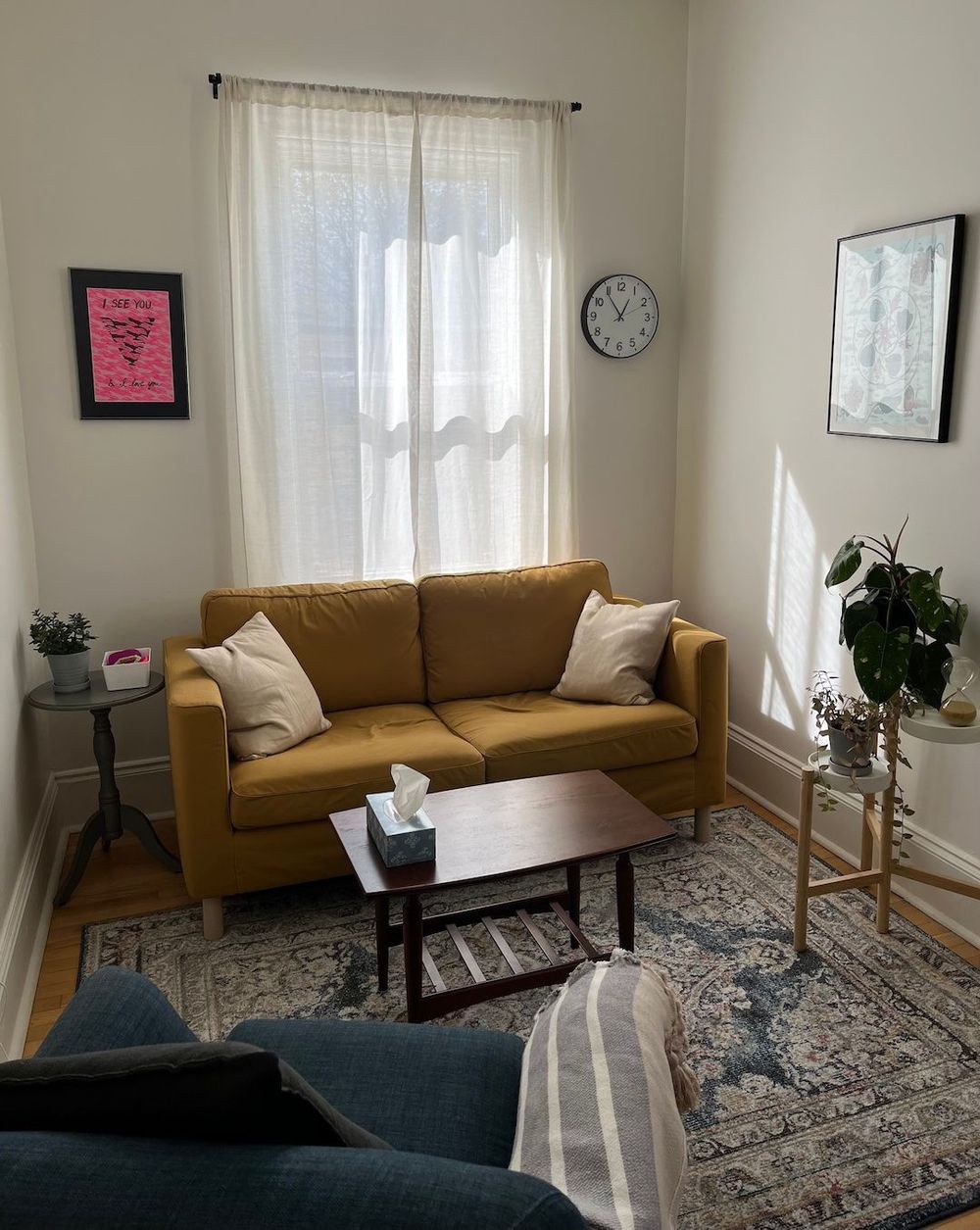 View of second floor office space in daylight with mustard-coloured couch, several plants, navy blue chair, and art on the walls.