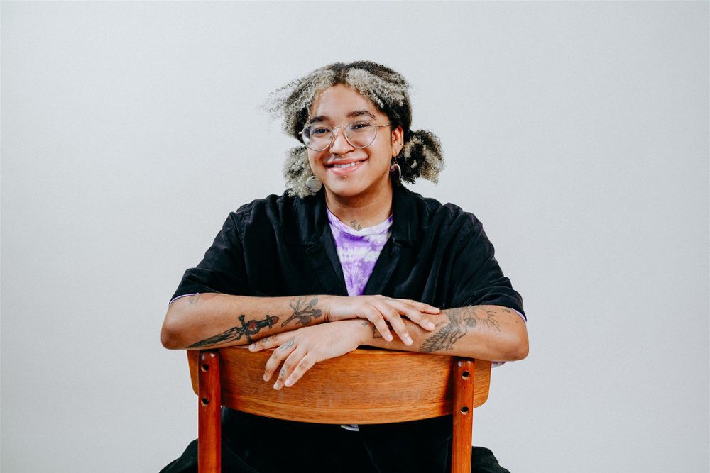 Jas smiling, sitting on a chair with its back facing the viewer. 
